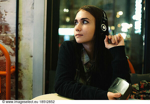 Young woman listening music in headphones sitting in cafe at night