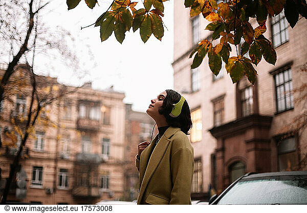 Young woman listening music in headphones standing on street in city