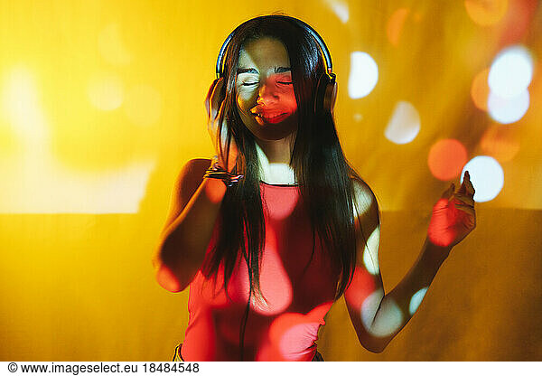 Young woman listening music on headphones over colored background