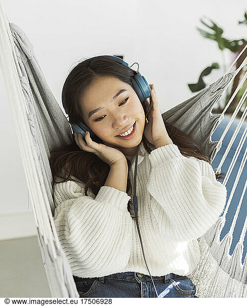 Young woman listening music through headphones on hammock at home