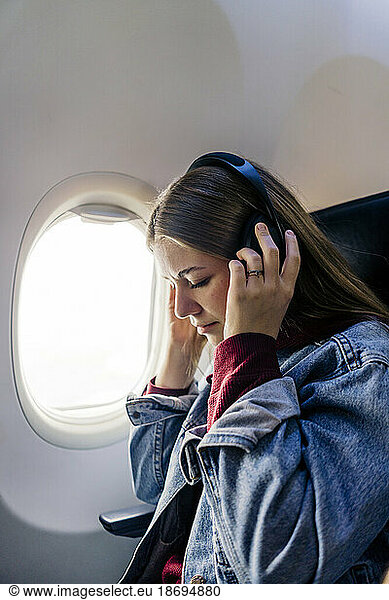 Young woman listening to music with headphones in airplane
