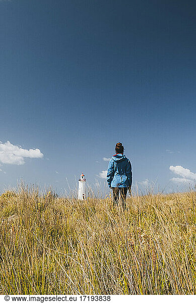 Young woman looking at a Lighthouse in the distance wearing blue jacket  Port Fairy  Australia.