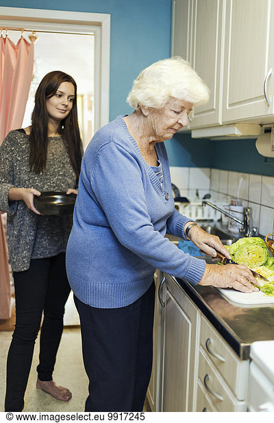 Young woman looking at grandmother preparing food in kitchen