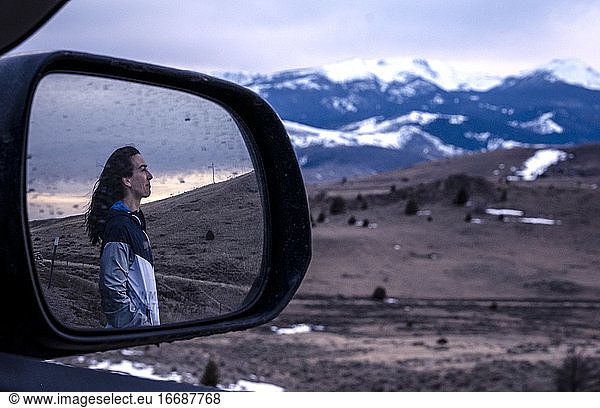 Young woman looking at sunset in the mountains reflected in mirror