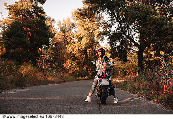 Young woman looking at sunset sitting on motorcycle on country road