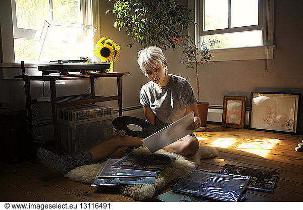 Young woman looking at vinyl records while sitting on floor at home