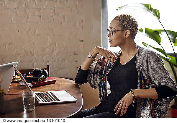 Young woman looking away while sitting at table with laptops