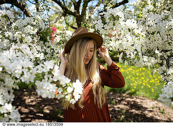 Young Woman Looking Down Holding Hat Surrounded by White Pear Flowers