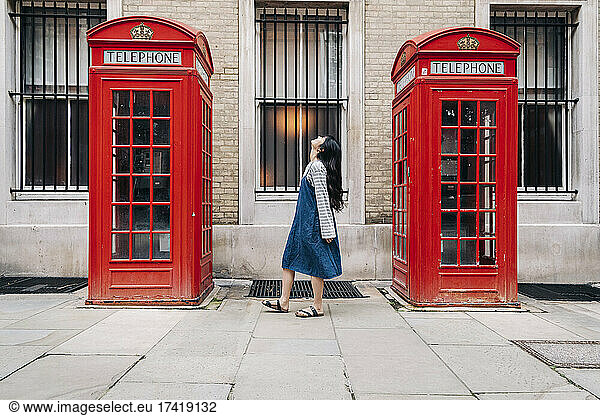 Young woman looking up while standing between telephone booth
