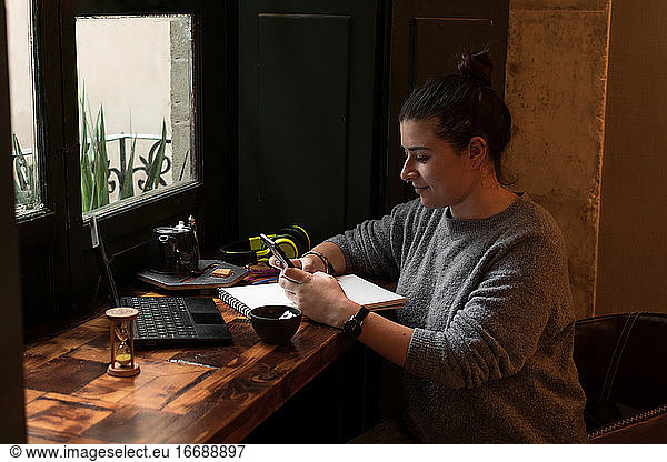 Young woman looks at her phone while studying in a retro pub
