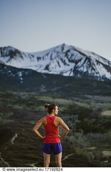 Young woman looks out at the mountains while trail running at dawn