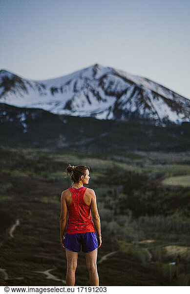 Young woman looks out at the mountains while trail running at dusk