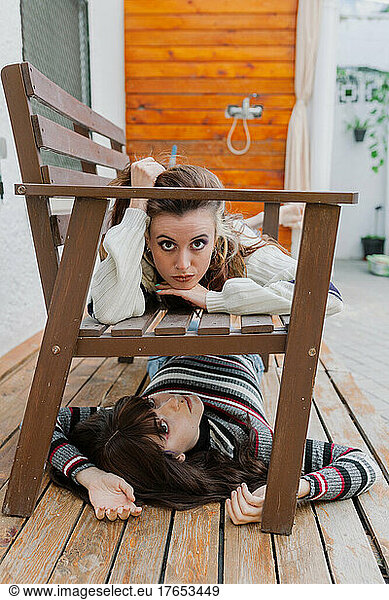 Young woman lying on bench over friend at back yard