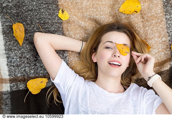 Young woman lying on blanket, covering eye with leaf
