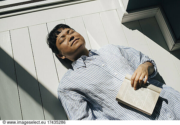 Young woman lying on floor with book in sunlight at home