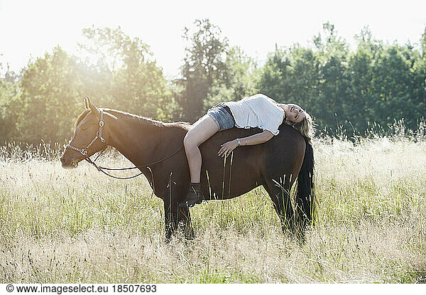 Young woman lying on her horse in farm and smiling  Bavaria  Germany