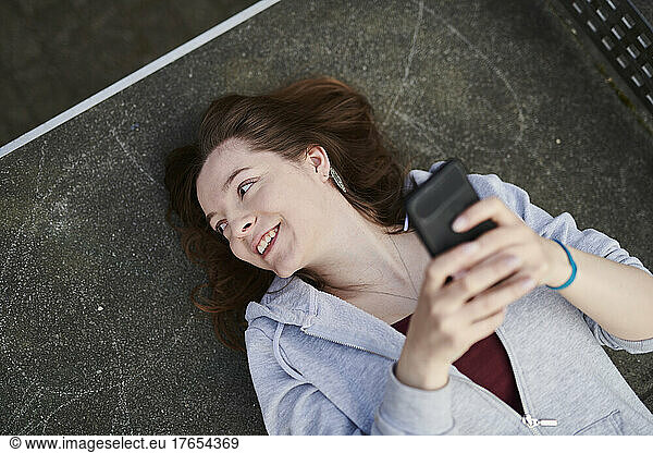 Young woman lying on table tennis table holding smartphone