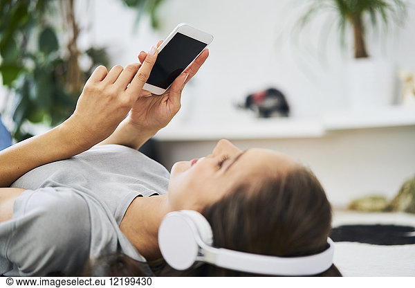Young woman lying on the floor with headphones and cell phone