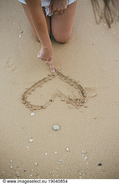 Young woman making a heart shape in sand