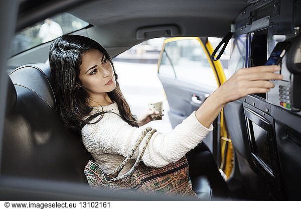Young woman making contactless payment through smart phone in taxi