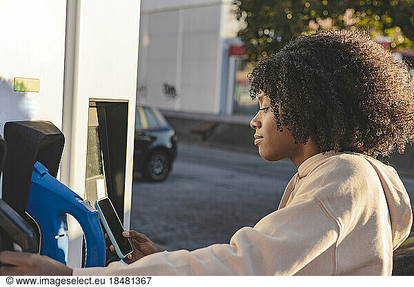 Young woman making payment through smart phone at electric vehicle charging station
