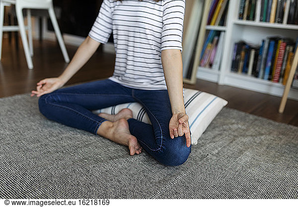 Young woman meditating while sitting on pillow at home