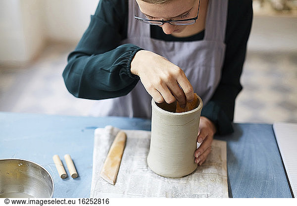 Young woman molding earthenware at table in art studio
