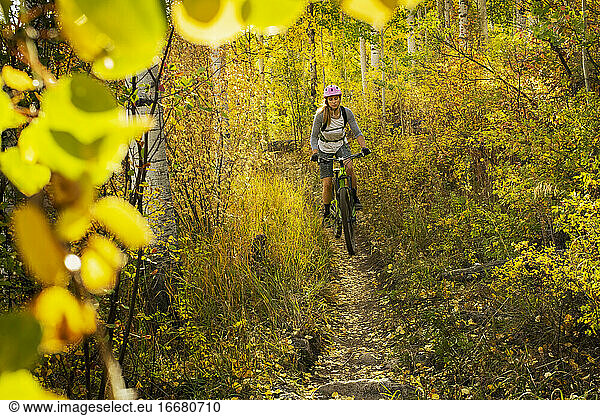 Young woman mountain biking amidst trees in forest during autumn