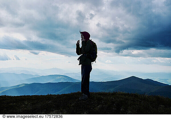Young woman mountain hiker on top of a mountain against a cloudy sky.