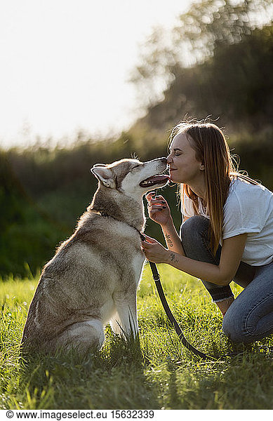Young woman nose to nose with her dog on a meadow