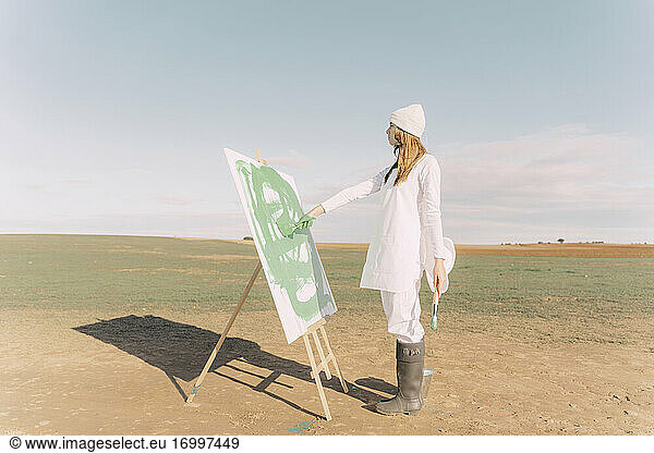 Young woman on dry field  painting canvas with green paint