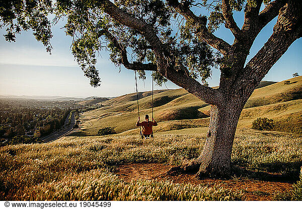 Young Woman on tree swing in rolling green hills