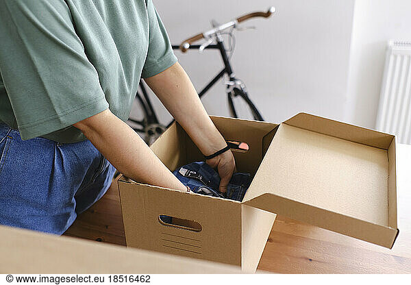 Young woman packing clothes in cardboard box