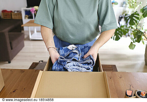 Young woman packing jeans in cardboard box at home