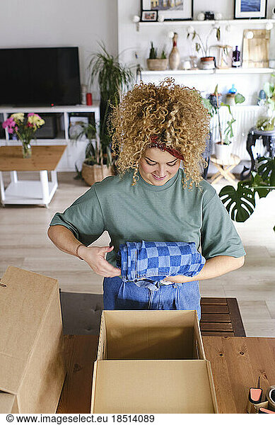 Young woman packing order in cardboard box at home