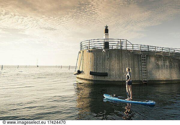 Young woman paddleboarding in sea by lighthouse