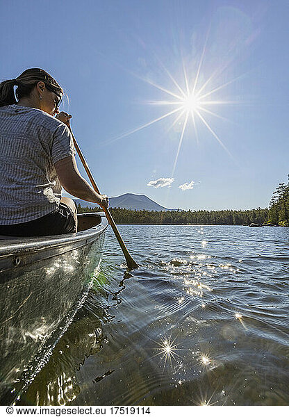 Young woman paddles canoe on Daicey Pond  Maine. Katahdin in distance.