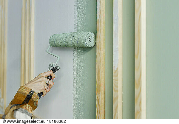 Young woman painting with paint roller on wall in apartment