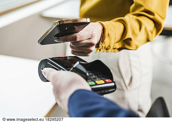 Young woman paying with smart phone on card reader machine