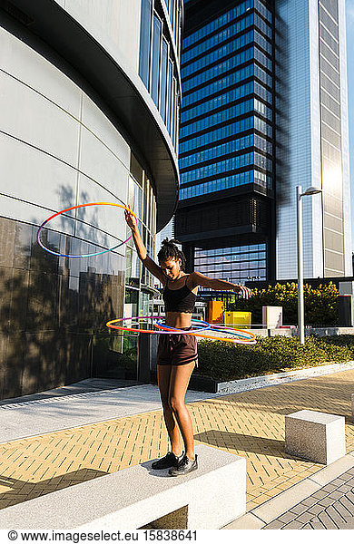 Young woman performing Hula Hoop dance with four rings in urban area