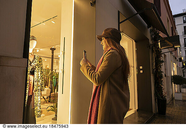Young woman photographing and doing window shopping at footpath
