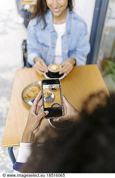 Young woman photographing food and drink through smart phone