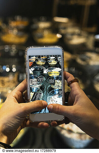 Young woman photographing food through mobile phone in retail store