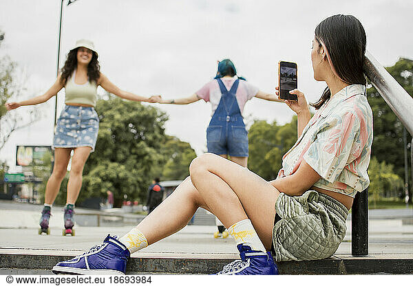 Young woman photographing friends roller skating at footpath