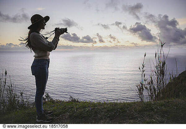 Young woman photographing through camera in front of sea