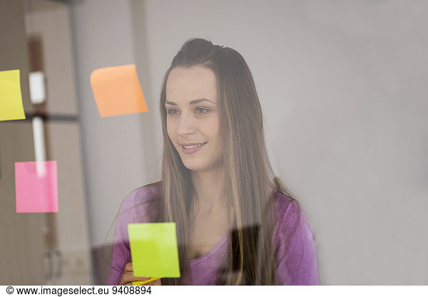 Young woman planning sticking post-its on glass
