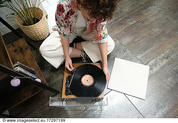 Young woman playing a vinyl record on a turntable at home