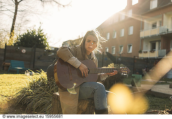 Young woman playing guitar in garden in sunshine