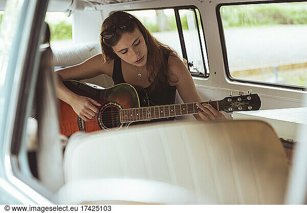 Young woman playing guitar while sitting in van during road trip