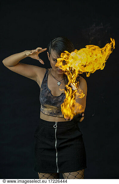 Young woman playing with fire against black background